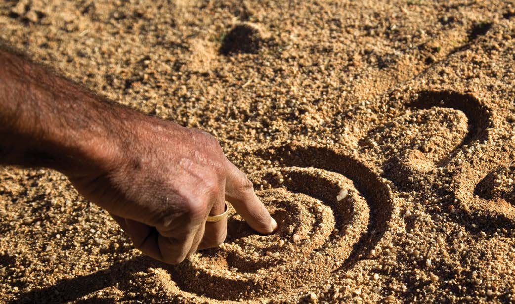 A hand drawing concentric circles in the sand